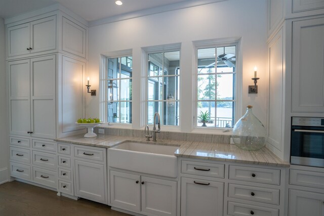 kitchen featuring sink, light stone countertops, oven, and white cabinets