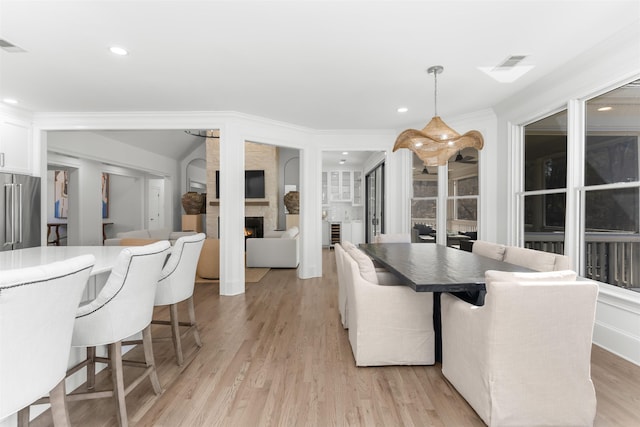 dining room with crown molding, a fireplace, recessed lighting, visible vents, and light wood-type flooring