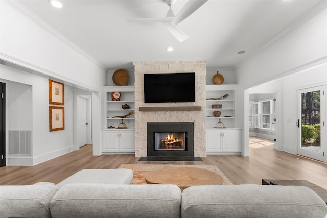 living room featuring visible vents, built in features, ornamental molding, a stone fireplace, and light wood-type flooring