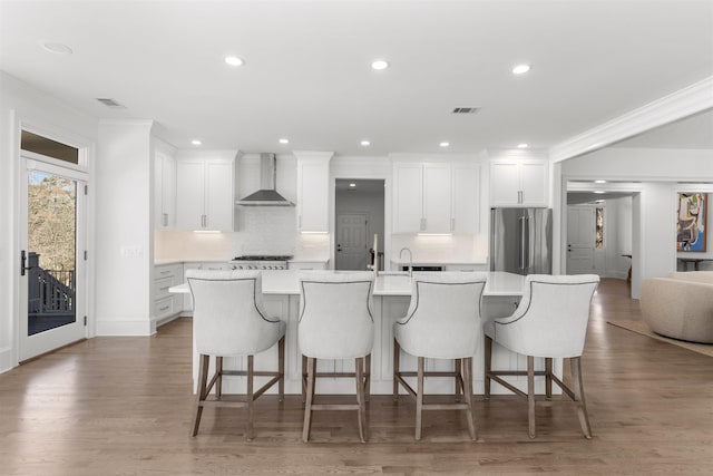 kitchen with visible vents, a spacious island, wall chimney exhaust hood, light countertops, and high end fridge