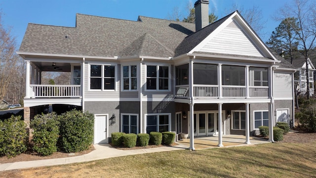 rear view of property featuring roof with shingles, a yard, a patio, a chimney, and a sunroom