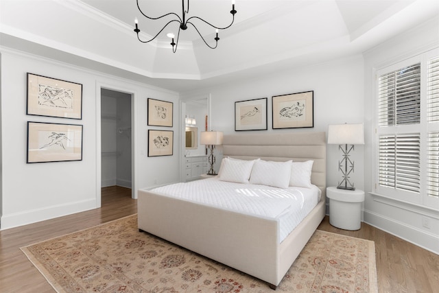bedroom featuring a tray ceiling, a notable chandelier, a spacious closet, ornamental molding, and wood finished floors