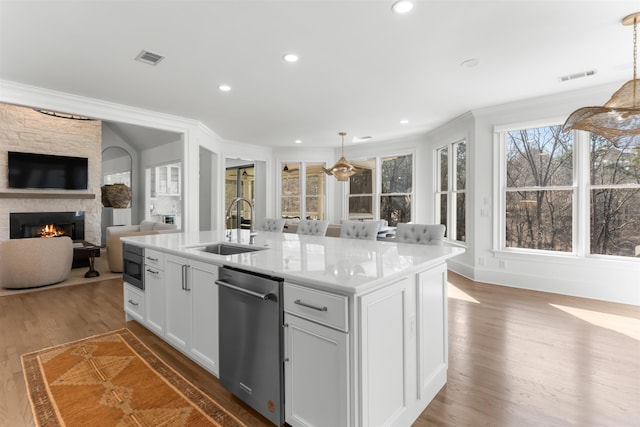 kitchen with visible vents, wood finished floors, a sink, a stone fireplace, and stainless steel dishwasher