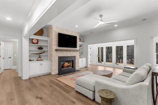 living area with ornamental molding, light wood-type flooring, a stone fireplace, and built in shelves