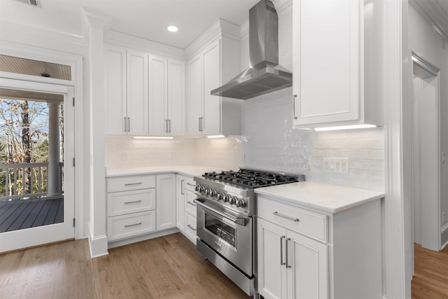 kitchen featuring stainless steel stove, light countertops, light wood-style floors, white cabinets, and wall chimney range hood