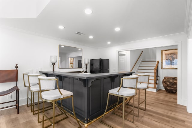 kitchen featuring light wood finished floors, visible vents, ornamental molding, freestanding refrigerator, and a kitchen bar