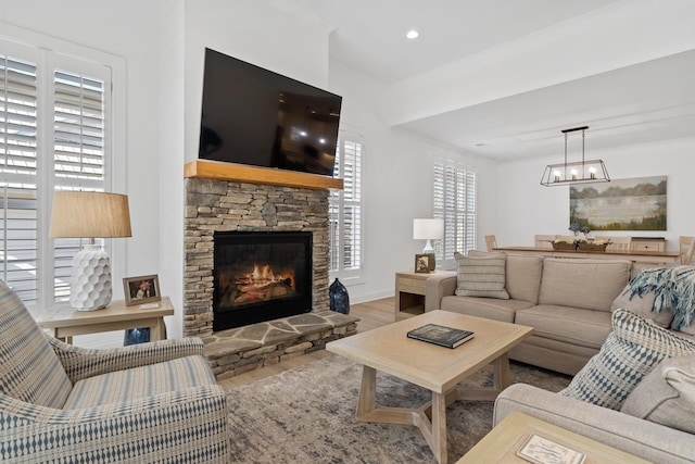 living room featuring baseboards, wood finished floors, a notable chandelier, and a stone fireplace