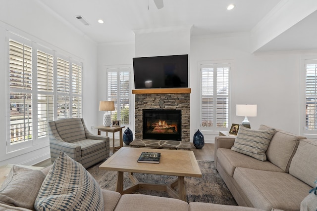 living area with visible vents, a stone fireplace, ceiling fan, crown molding, and wood finished floors