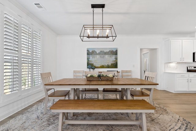 dining room with light wood finished floors, a notable chandelier, visible vents, and crown molding