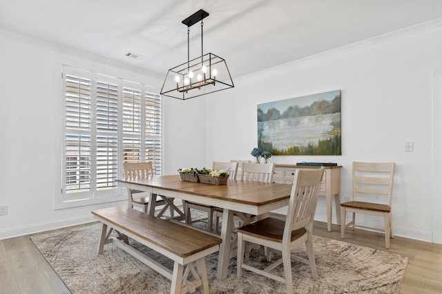 dining room featuring baseboards, light wood-type flooring, ornamental molding, a chandelier, and visible vents