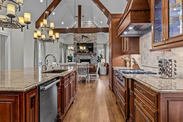 kitchen with sink, hanging light fixtures, vaulted ceiling with beams, light stone countertops, and a large island with sink