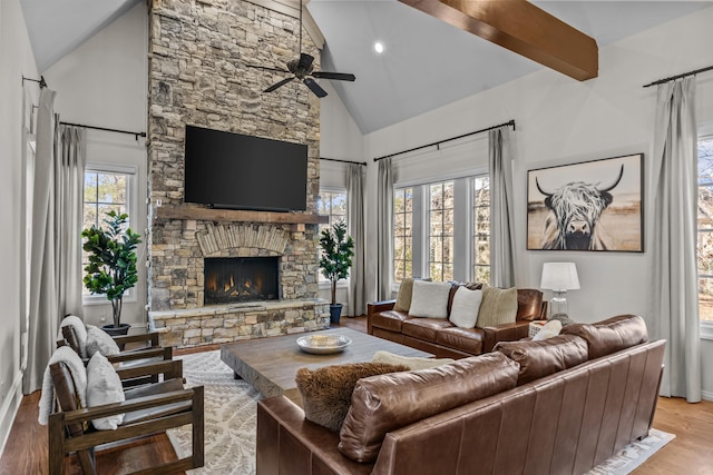 living room featuring beamed ceiling, a stone fireplace, high vaulted ceiling, and light wood-type flooring