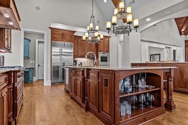 kitchen featuring premium range hood, lofted ceiling, appliances with stainless steel finishes, hardwood / wood-style floors, and a kitchen island with sink