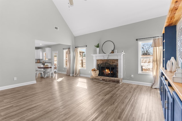 unfurnished living room with ceiling fan, a brick fireplace, high vaulted ceiling, and light hardwood / wood-style flooring