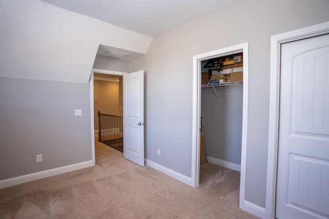 unfurnished bedroom featuring light carpet, a spacious closet, vaulted ceiling, and a closet