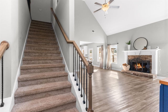 stairway featuring hardwood / wood-style floors, high vaulted ceiling, a brick fireplace, and ceiling fan