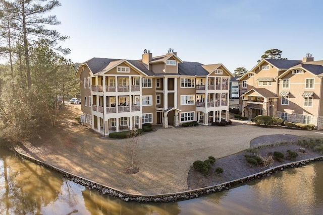 exterior space with a chimney, a water view, a residential view, and a balcony