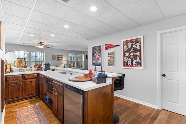 kitchen with a peninsula, a paneled ceiling, wood finished floors, light countertops, and ceiling fan