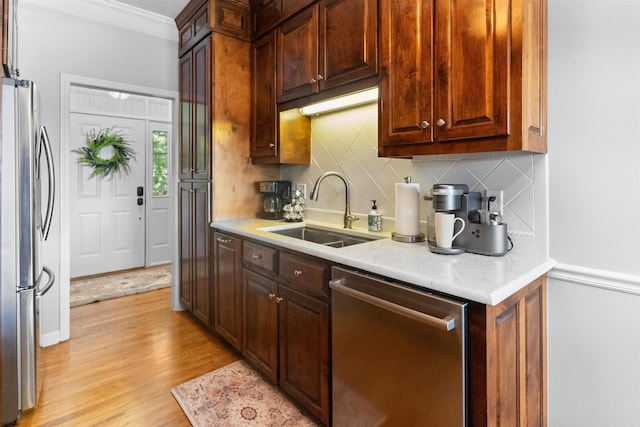 kitchen with appliances with stainless steel finishes, a sink, crown molding, light wood-type flooring, and tasteful backsplash