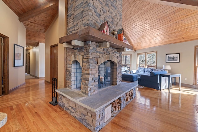 living room featuring light wood finished floors, baseboards, wooden ceiling, a stone fireplace, and beam ceiling