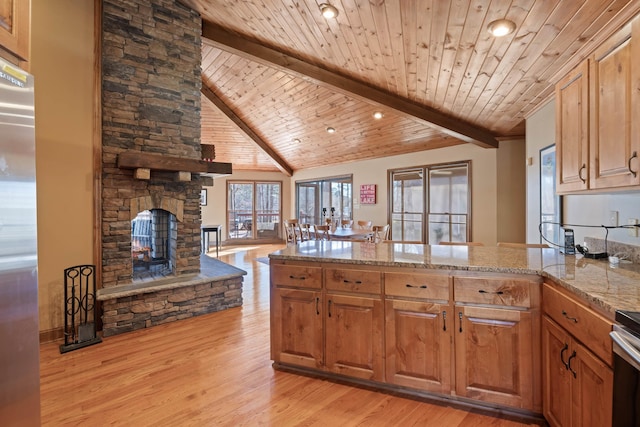 kitchen with light stone counters, a peninsula, light wood-style floors, beamed ceiling, and stainless steel fridge