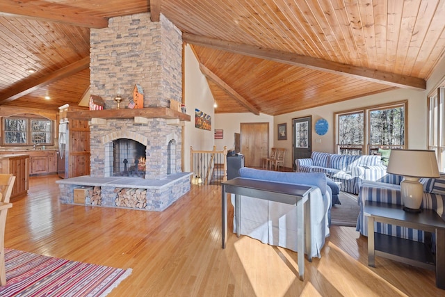 living area with wooden ceiling, light wood-style flooring, beamed ceiling, and a stone fireplace