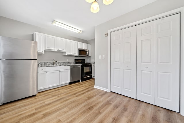 kitchen with light wood-type flooring, light stone counters, stainless steel appliances, white cabinetry, and a sink