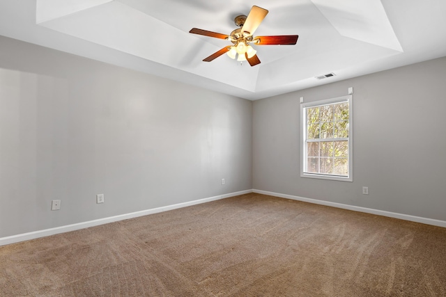 carpeted spare room with a ceiling fan, a tray ceiling, baseboards, and visible vents