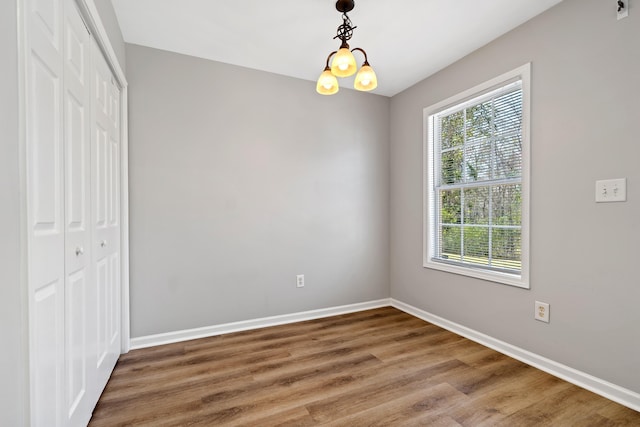 unfurnished bedroom featuring an inviting chandelier, wood finished floors, baseboards, and a closet