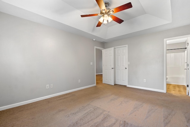 unfurnished bedroom featuring a raised ceiling, a ceiling fan, connected bathroom, carpet floors, and baseboards