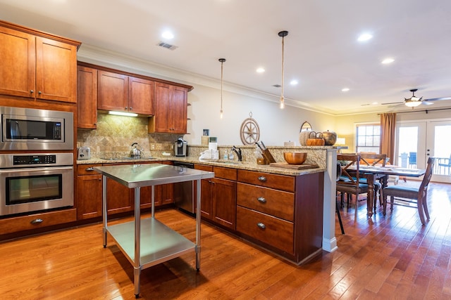 kitchen featuring appliances with stainless steel finishes, pendant lighting, wood-type flooring, decorative backsplash, and kitchen peninsula