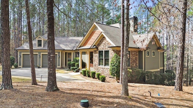 view of front facade featuring stone siding, a chimney, an attached garage, and driveway