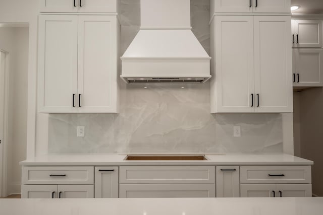 kitchen featuring custom exhaust hood, light countertops, backsplash, white cabinetry, and black electric cooktop