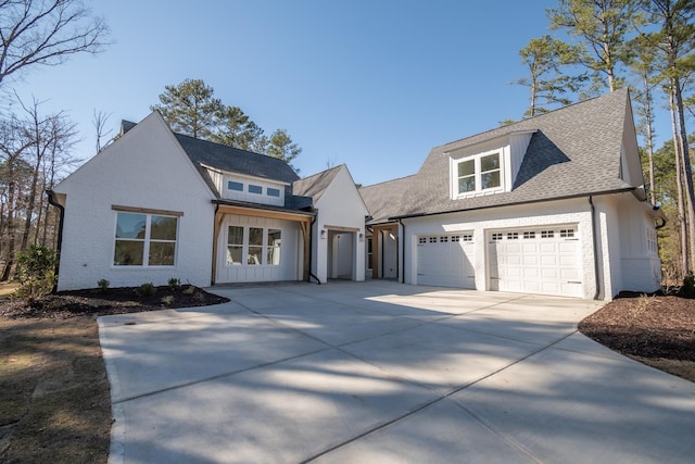 modern farmhouse style home featuring concrete driveway, brick siding, an attached garage, and roof with shingles