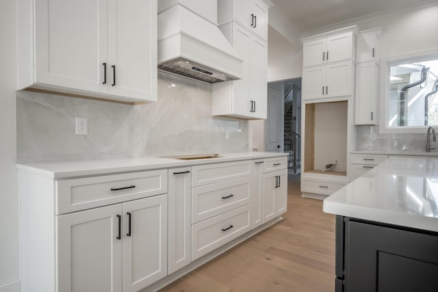 kitchen featuring light countertops, custom range hood, light wood-style flooring, backsplash, and white cabinetry