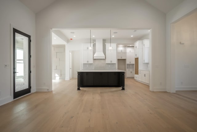 kitchen with lofted ceiling, custom range hood, light wood finished floors, and white cabinetry