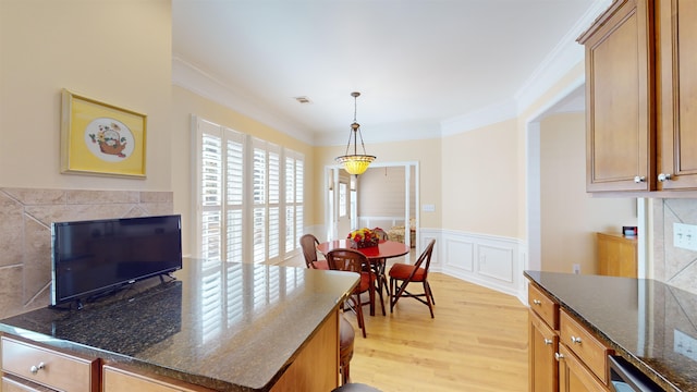 kitchen featuring pendant lighting, crown molding, dark stone counters, and light wood-type flooring