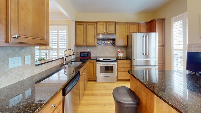 kitchen featuring appliances with stainless steel finishes, sink, backsplash, dark stone counters, and light hardwood / wood-style floors