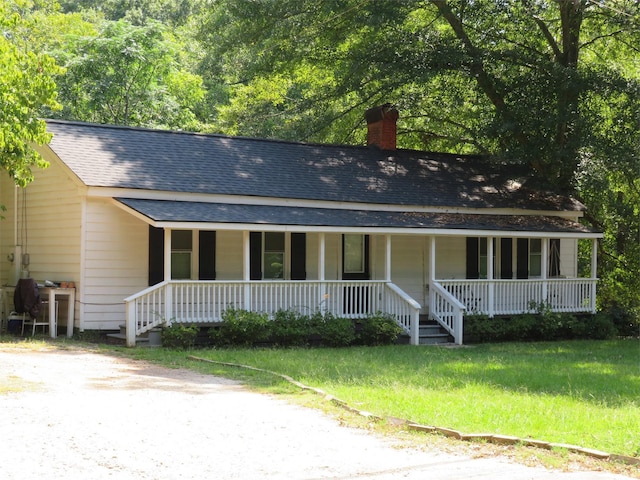 view of front facade featuring a shingled roof, a chimney, and a porch