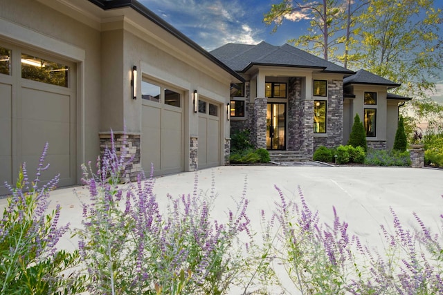 prairie-style house with an attached garage, concrete driveway, stone siding, and stucco siding