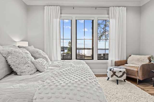 bedroom featuring a water view, wood finished floors, and baseboards