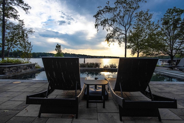 patio terrace at dusk featuring a water view and an outdoor pool