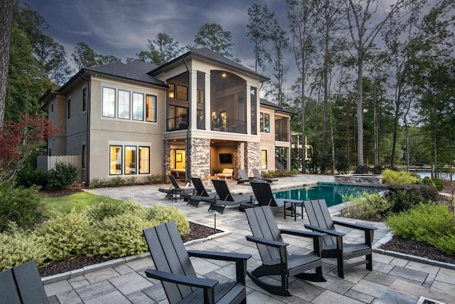 rear view of property featuring a patio, stone siding, a fireplace, and a sunroom