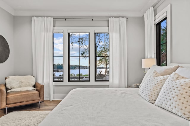 bedroom with a water view, crown molding, baseboards, and wood finished floors