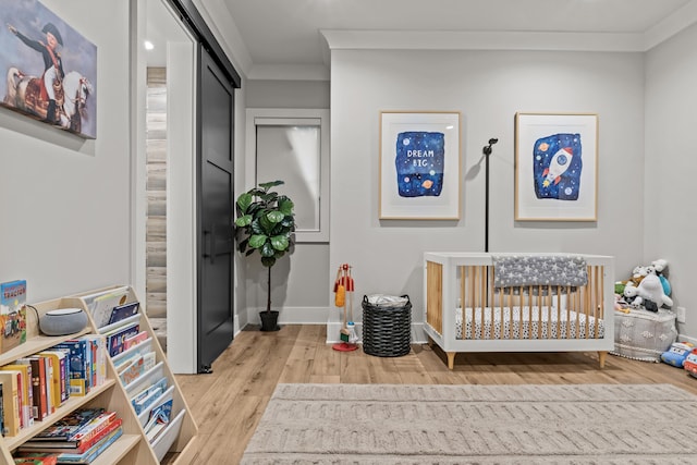 bedroom with ornamental molding, a nursery area, light wood-style floors, and baseboards