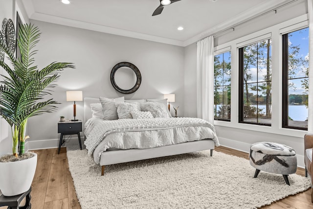 bedroom featuring baseboards, wood finished floors, a water view, crown molding, and recessed lighting