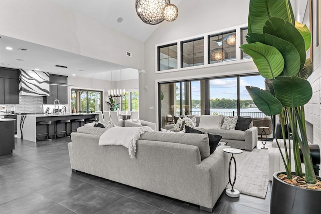 living area featuring plenty of natural light, high vaulted ceiling, a water view, and an inviting chandelier