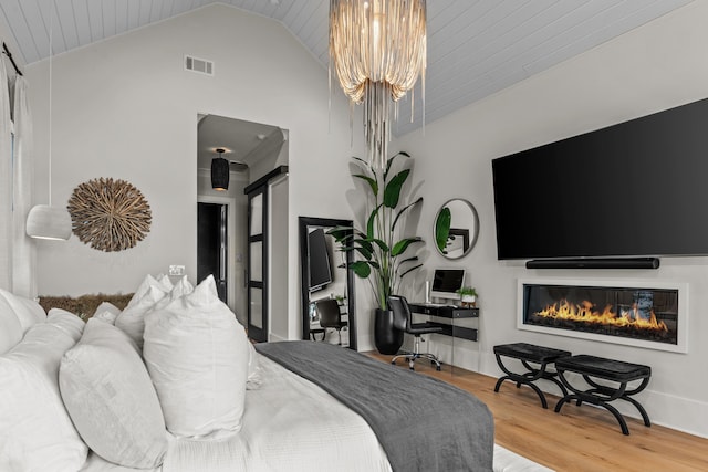 bedroom with a barn door, visible vents, a glass covered fireplace, wood finished floors, and a chandelier