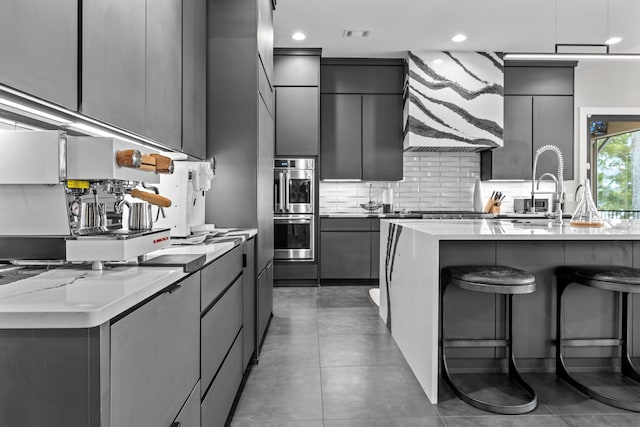 kitchen featuring a breakfast bar area, decorative backsplash, gray cabinetry, appliances with stainless steel finishes, and modern cabinets