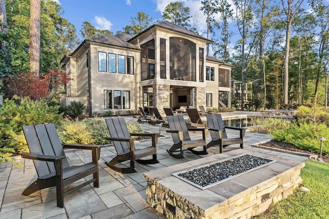 back of house featuring a sunroom, an outdoor fire pit, a patio area, and a fireplace